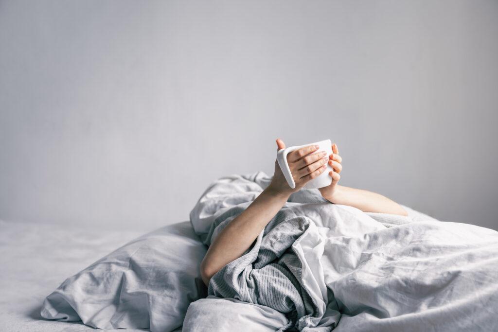 womans hand holds cup coffee while lying bed